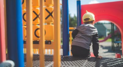 child sitting at the top of a red slide on a playground